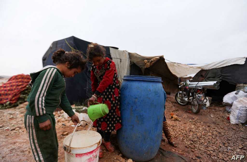 Children on November 20, 2021, fill a bucket with water, in the Bardaqli camp for displaced people in the town of Dana in Syria's northwestern Idlib province, as winter approaches on the International Day of Children's Rights. (Photo by AAREF WATAD / AFP)